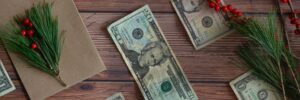 closeup of $20 bill on wood table with holly sprigs
